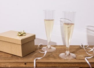 Værtindegave: hvad man tager med, og hvad værten faktisk kan bruge Indpakket gaveæske med guldsløjfe ved siden af to glas mousserende vin på et træbord